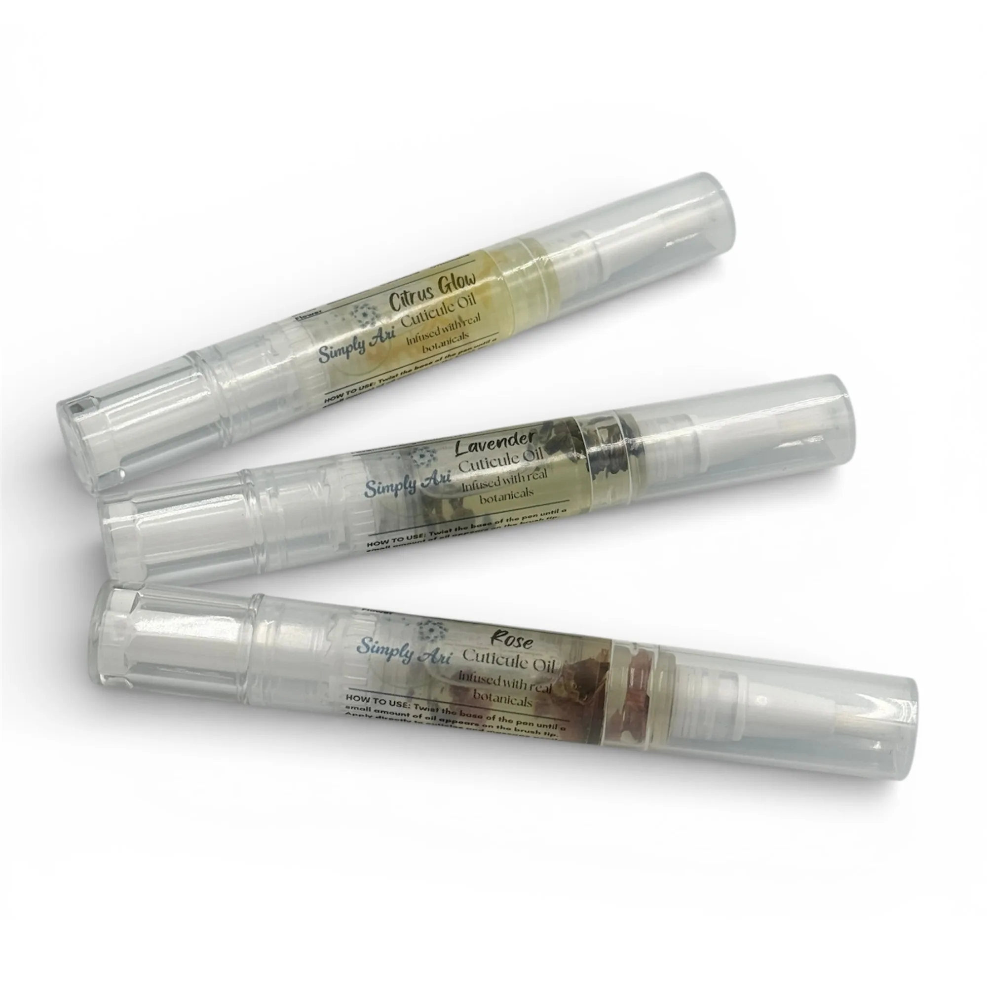 Three Simply Ari Cuticle Oil Pens in Citrus Glow, Lavender, and Rose with real botanicals in clear twist applicators