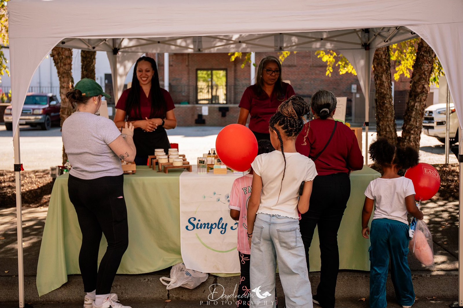 Simply Ari booth at an outdoor market with vendors and customers browsing skincare products